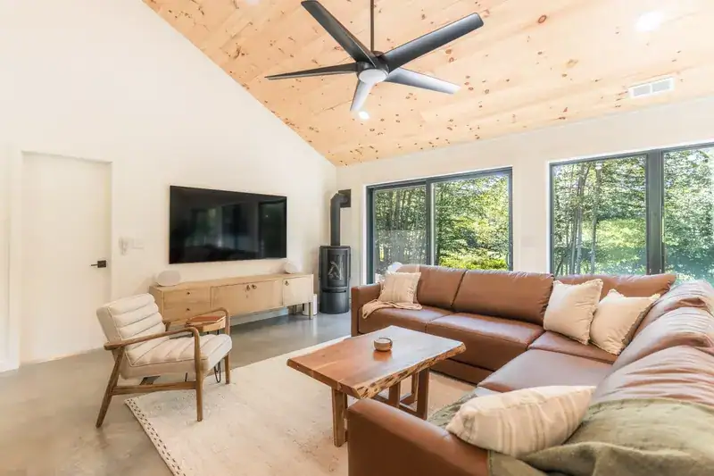Sectional sofa and armchair beside forest-facing windows